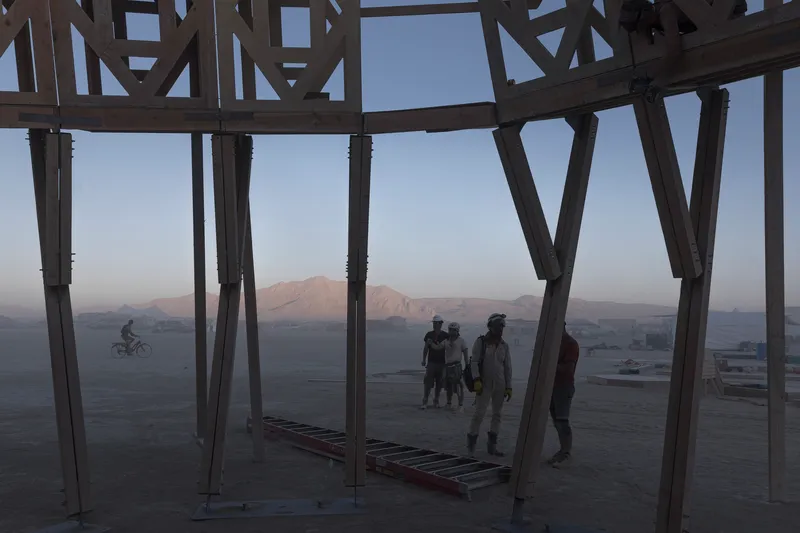 Interior view through angled timber columns framing visitors and distant mountains at twilight