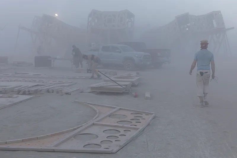 Curved perforated plywood roof panels laid out on the ground during construction in heavy fog