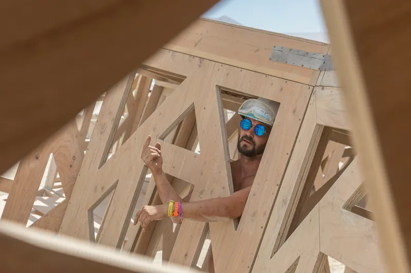 View through triangular plywood openings showing a builder working on the structural framework