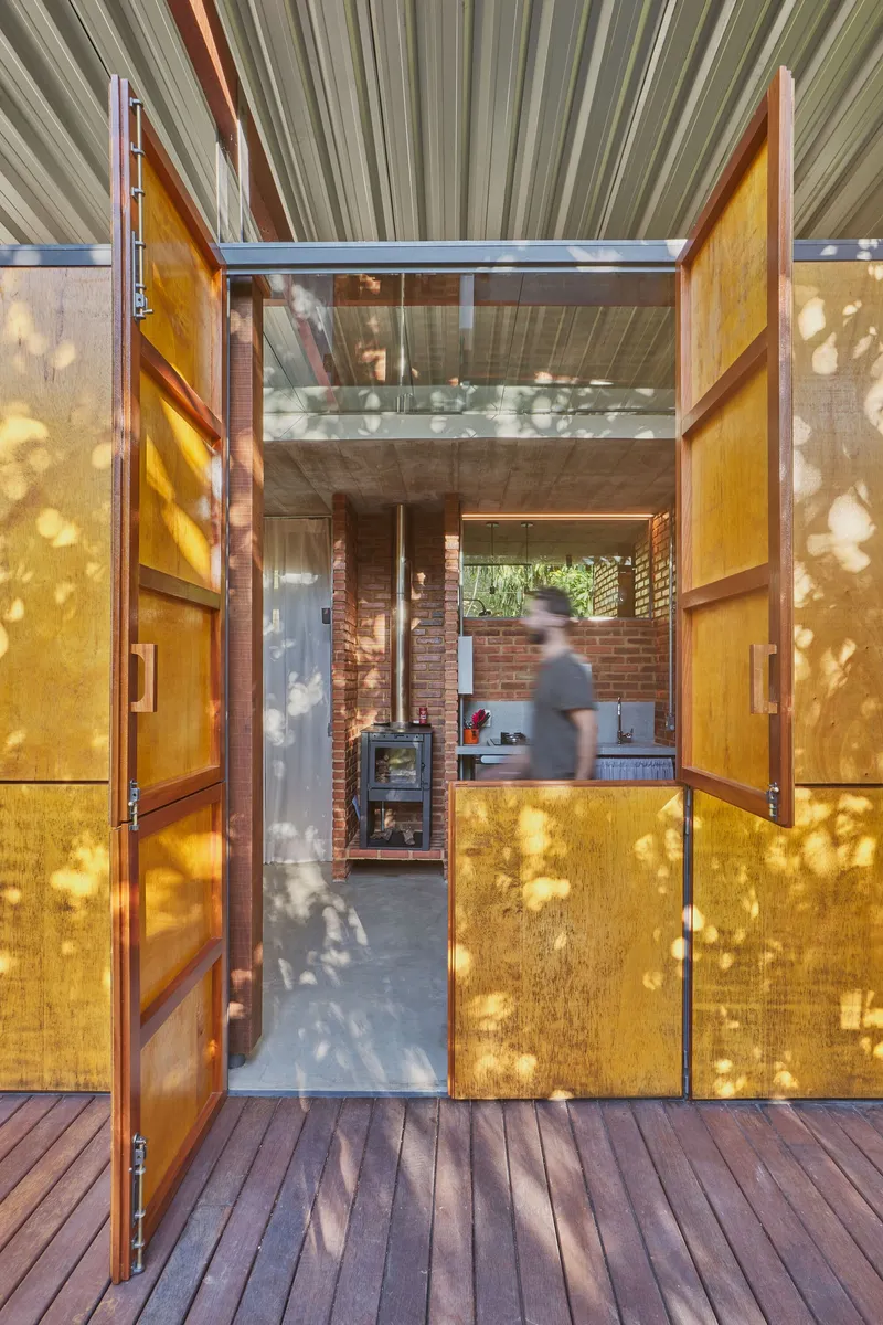 Open yellow timber doors framing view through to kitchen with wood stove and person