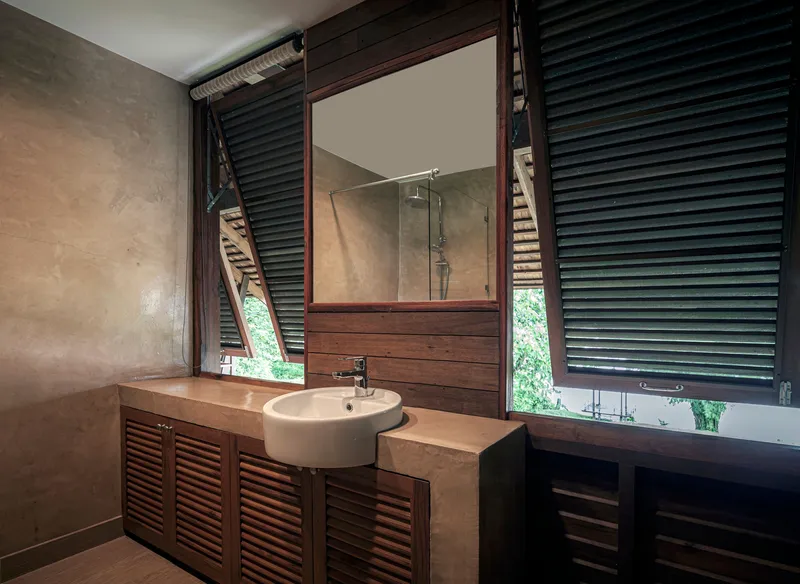 Bathroom vanity with white basin on louvered timber cabinetry below horizontal slatted shutters and mirror