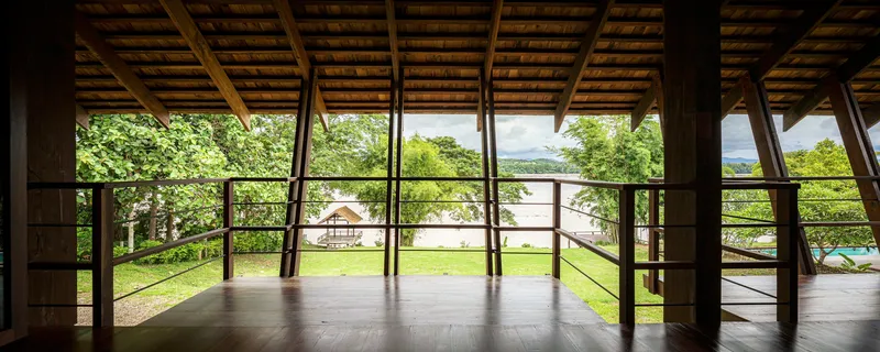 Upper floor terrace with steel railing overlooking lawn and water beyond under timber beam ceiling