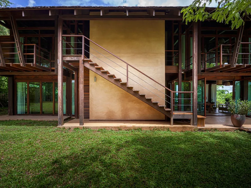 Exterior staircase with steel railings ascending against a polished plaster wall beneath the elevated timber structure
