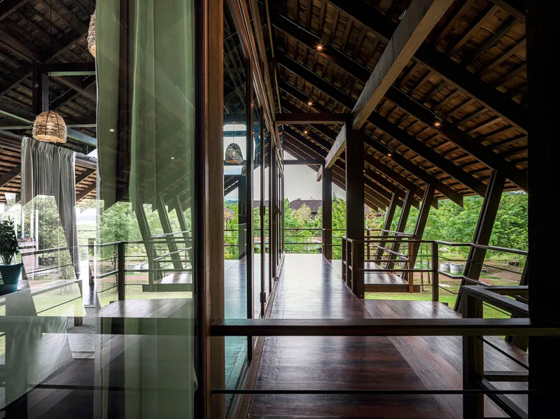 Corridor with dark timber floors and green glass partitions under a pitched roof with exposed timber trusses