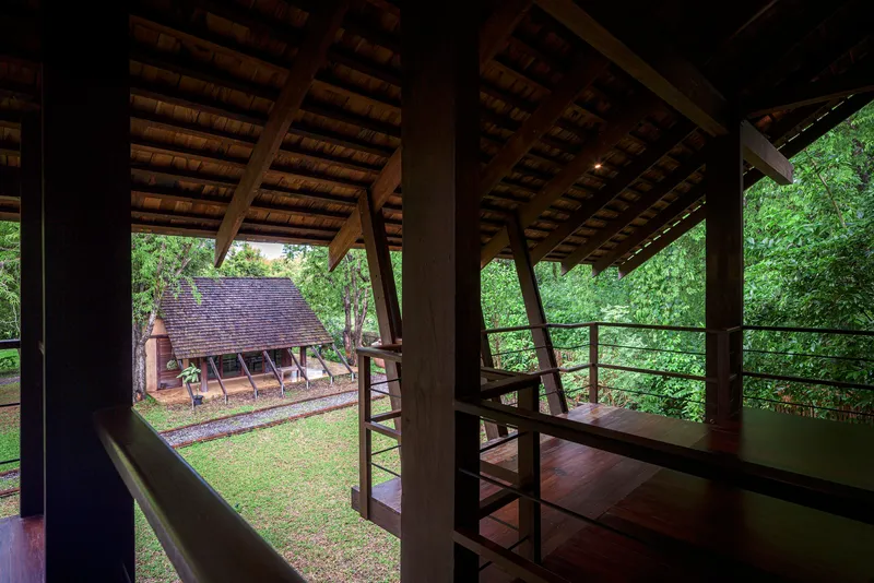 Interior looking through timber columns and steel railings to neighboring gabled structure in garden
