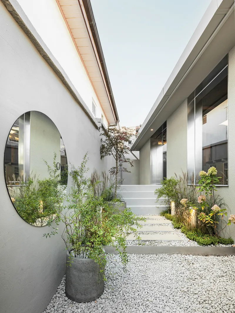 Courtyard with gravel and stone pavers, planted beds, and a small tree between two volumes