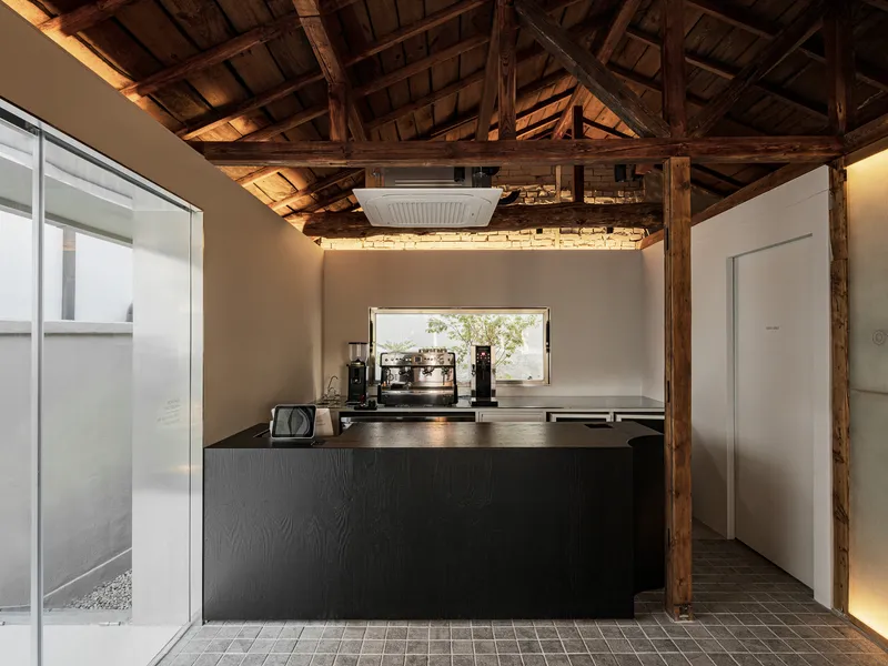 Dark oak kitchen island with espresso equipment beneath exposed timber beams and a horizontal window framing greenery