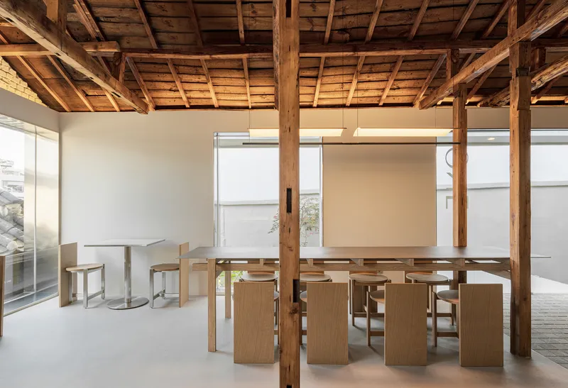 Communal dining tables and chairs arranged among timber columns under a vaulted timber ceiling with daylight filtering through translucent screens