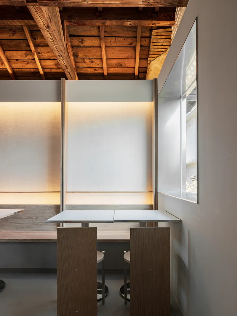 Close-up of a corner table beneath backlit wall panels and weathered timber ceiling joists casting shadows