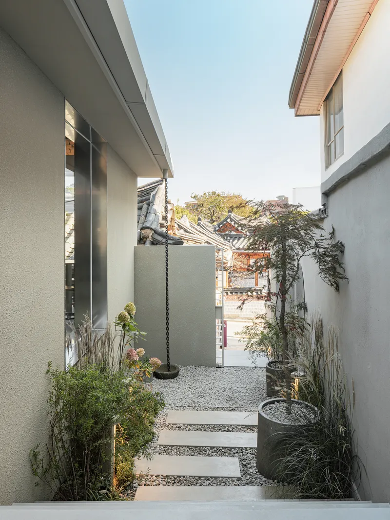 Narrow courtyard with gravel stepping stones, potted plants and a view toward traditional tiled roofs