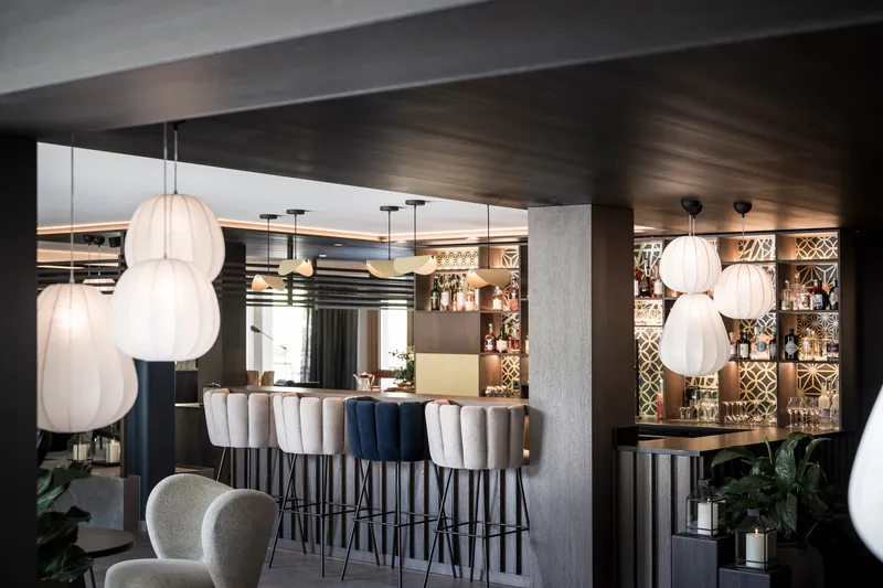 Bar area with upholstered stools, spherical pendant lights, and backlit geometric tile wall behind bottles