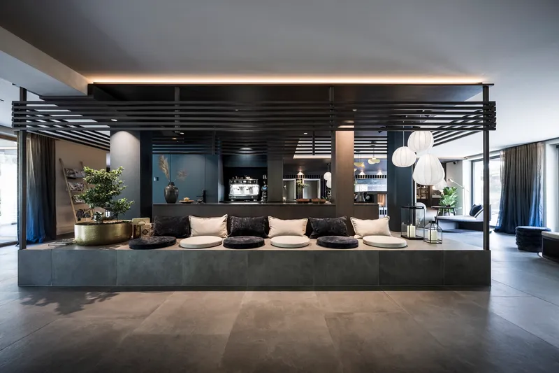 Hospitality bar with horizontal slatted canopy, dark stone counter and pendant lighting under grey ceiling