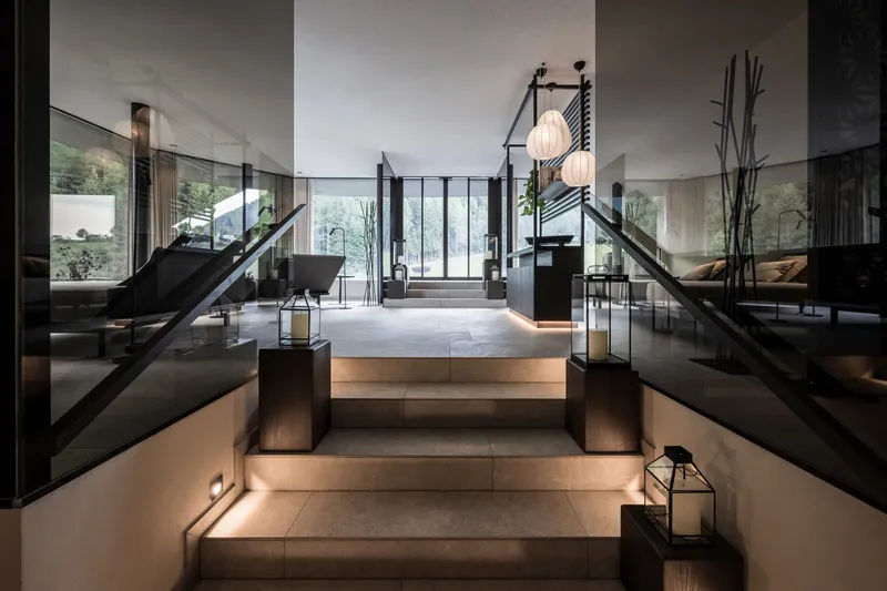 Illuminated stone staircase with glass railings ascending toward glazed entrance vestibule in evening light
