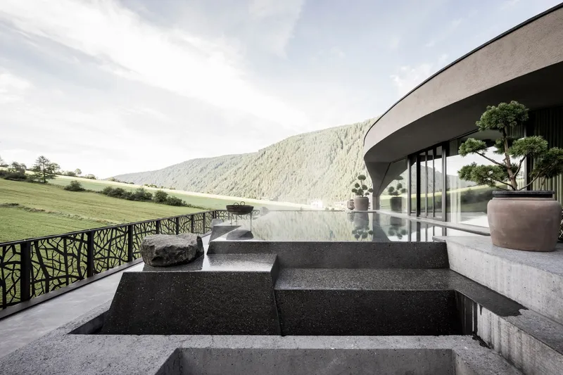 Cascading black stone fountain steps beneath curved canopy with glass walls and potted bonsai trees