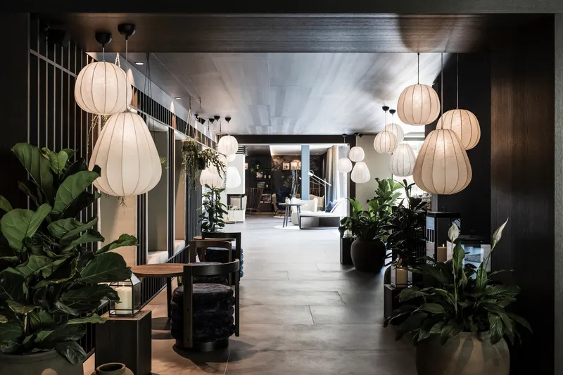 Lobby corridor with dark timber paneling, fabric pendant lamps and potted tropical plants