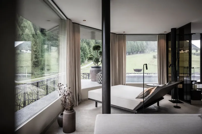 Spa room with freestanding white tub and floor-to-ceiling windows framing green meadow views