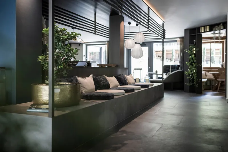 Lounge area with concrete seating platform, horizontal metal screen and brass planters under overcast daylight