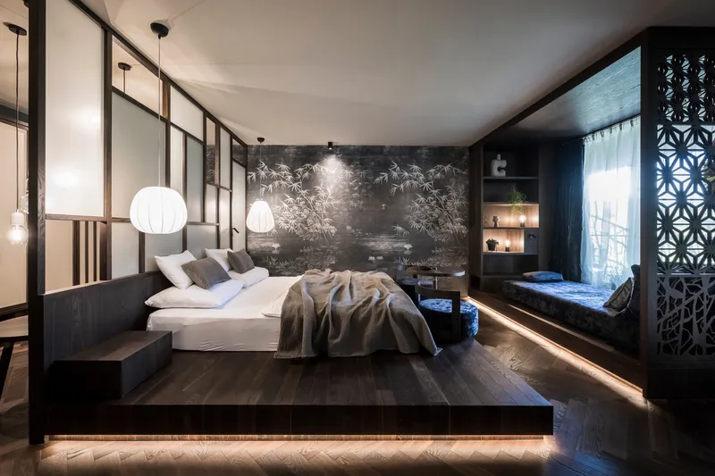 Platform bed with underlit perimeter set against dark botanical wallpaper under pendant globe fixtures