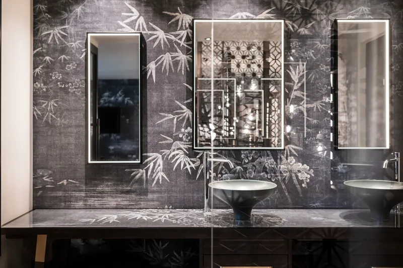 Twin mirrors with brass frames mounted on botanical chinoiserie wallcovering above marble vanity counter