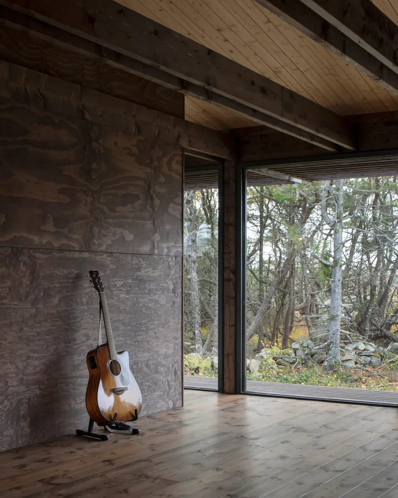 Corner of room with acoustic guitar leaning against marbled plywood wall beside glazed door to landscape