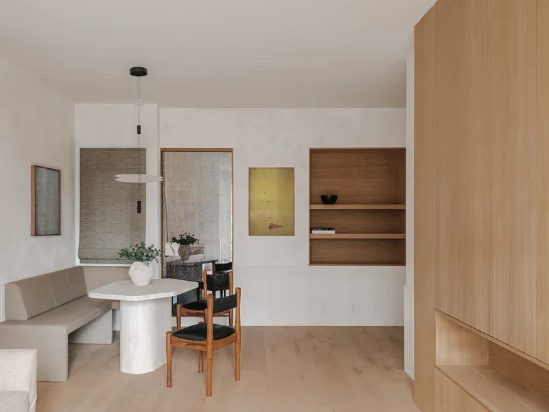Open dining area with cylindrical table, built-in banquette and recessed timber shelving niche