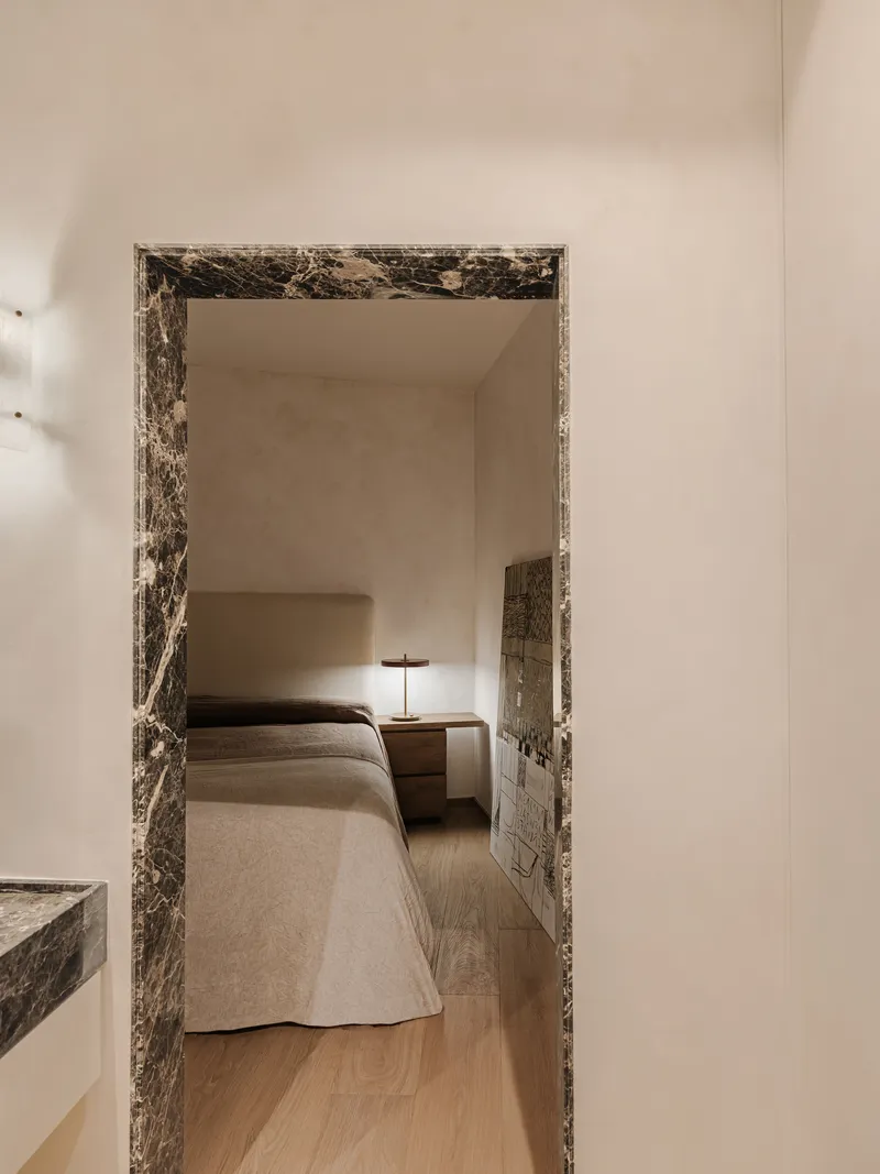 Bedroom viewed through a dark veined marble door frame with nightstand and lamp