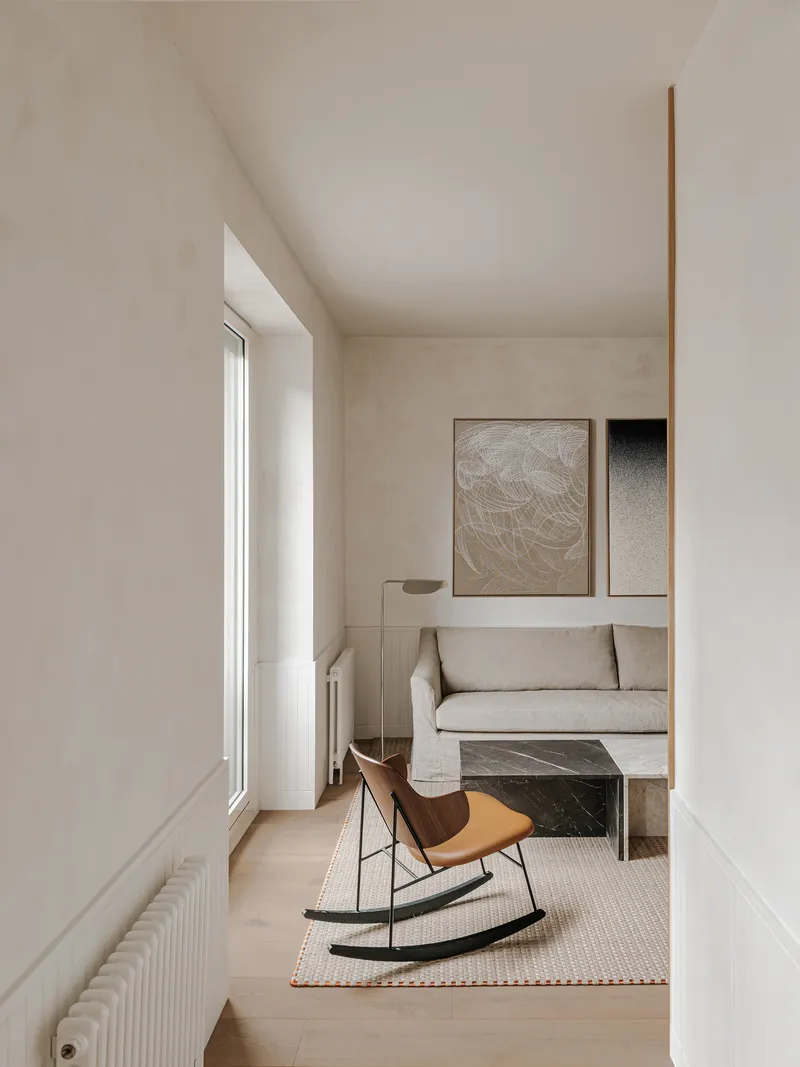 Living room with pale timber flooring, tall window, and leather rocking chair on a cream rug