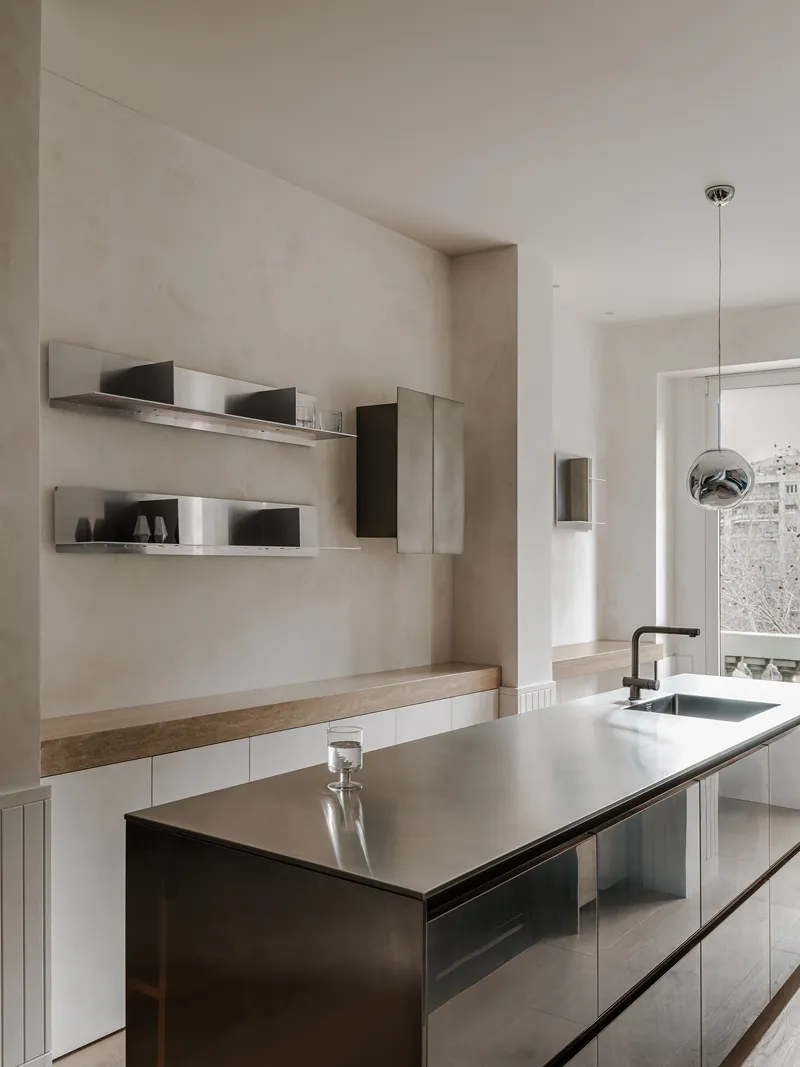 Kitchen island with dark reflective cabinetry and stainless steel countertop under a spherical pendant