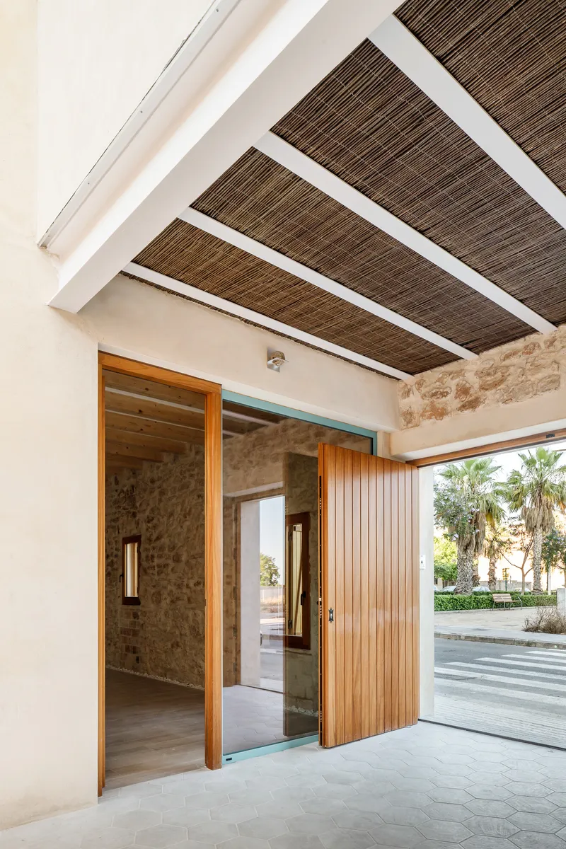 Covered entry porch with slatted timber ceiling panels and vertical wood cladding door facing palm trees