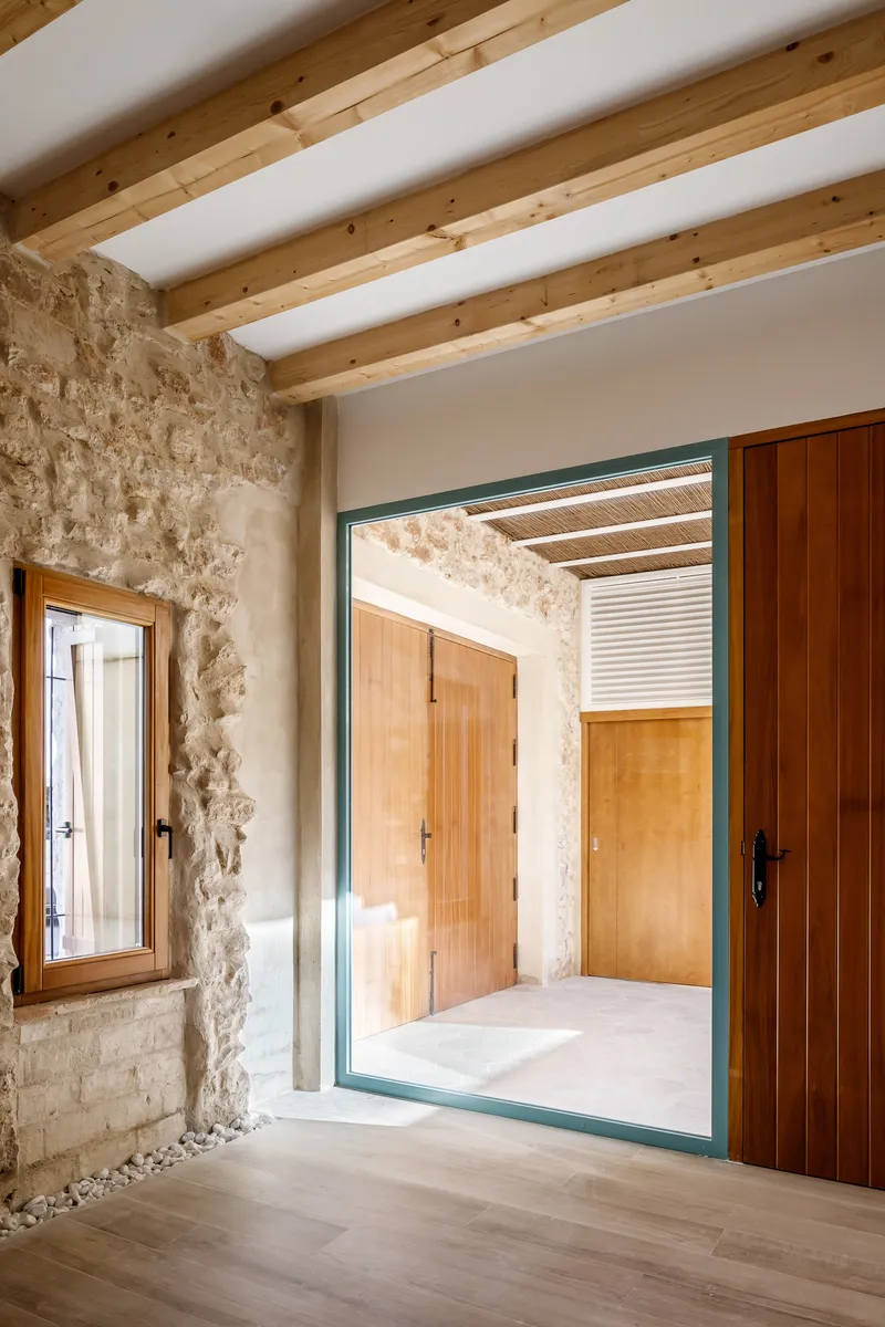 View through green steel-framed glass door into courtyard with exposed stone walls and timber slatted ceiling