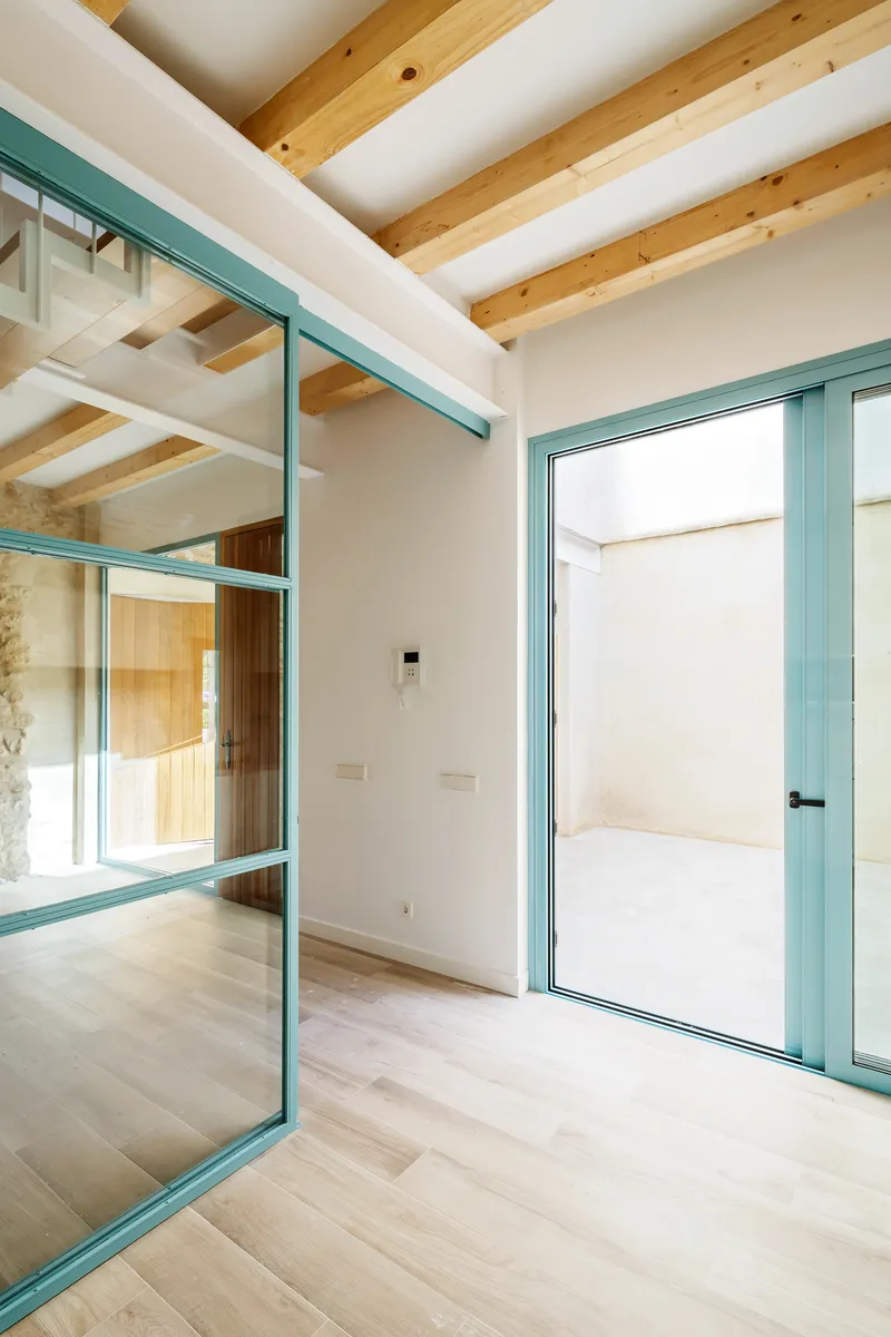Interior room with teal-framed glazing, exposed timber ceiling beams, and light wood flooring