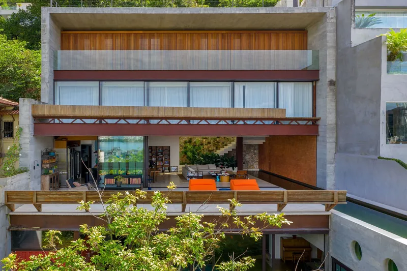 Stacked concrete terraces with timber screens and orange furniture overlooking tropical vegetation