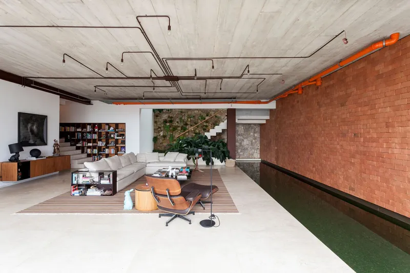 Living room with exposed concrete ceiling and red brick wall alongside interior pool