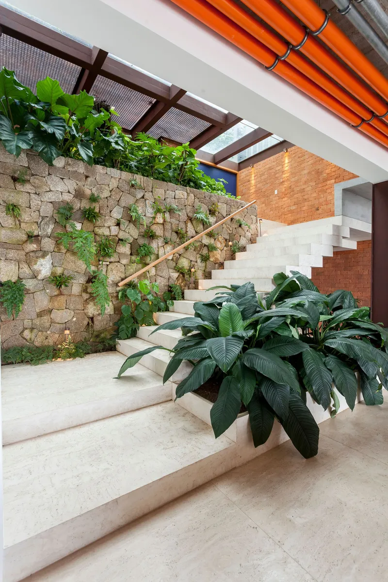 Stone wall staircase with cascading plants and brass handrail under exposed orange conduits