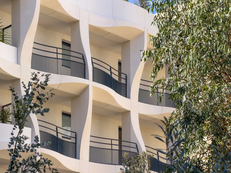 Curved balcony soffits with vertical metal railings framed by eucalyptus foliage