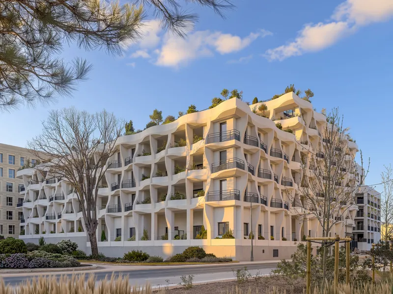 Street view of the undulating white facade with planted balconies framed by bare winter trees