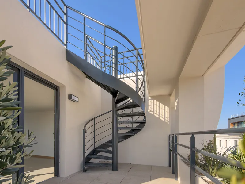 Exterior spiral stair with metal railings connecting balcony levels in bright sunlight