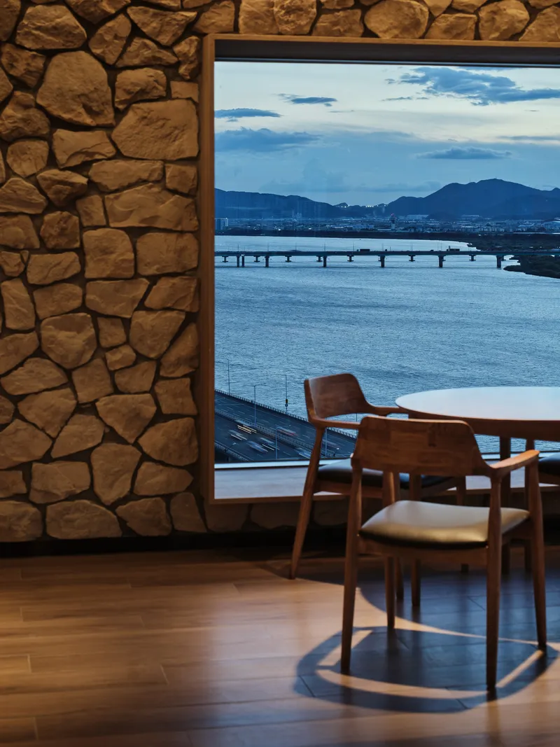 Framed window overlooking a river and distant mountains with timber chairs in the foreground