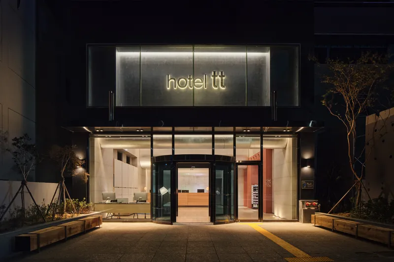 Hotel entrance with glass revolving door and illuminated signage at night with planted beds