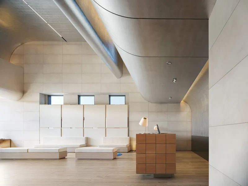 Interior lobby with curved stainless steel ductwork crossing above pale wood paneling and reception desk