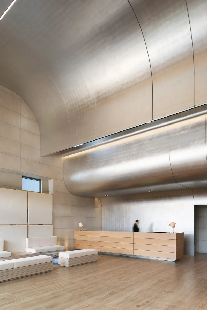 Reception area showing brushed metal duct running horizontally through double-height space with blurred figures