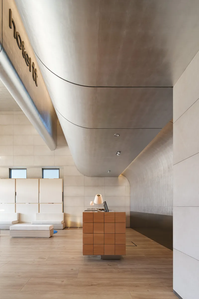 Detail of curved metal duct meeting wood-paneled wall above reception desk with layered platforms