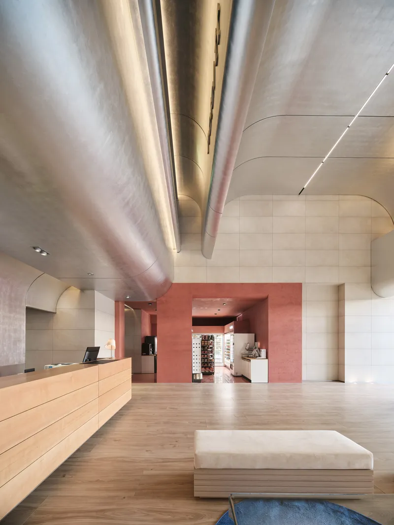 Reception lobby with light wood desk, curved metal ductwork overhead, and terracotta portal beyond