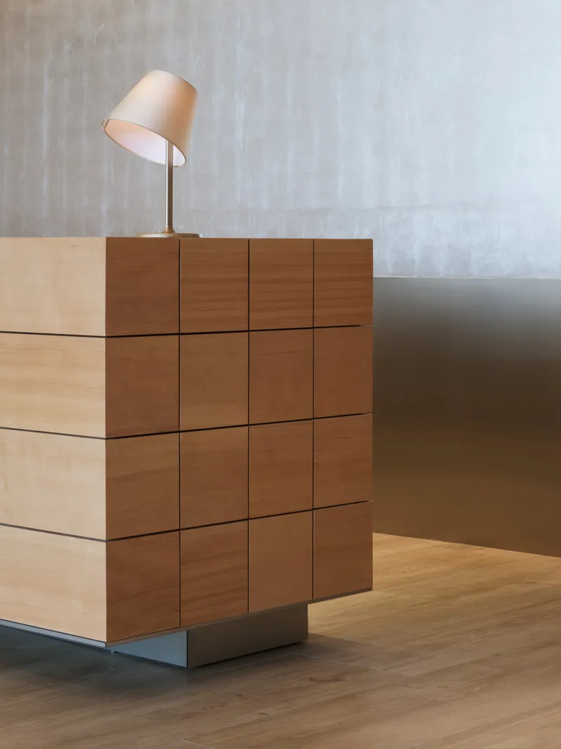 Stepped timber block reception desk with table lamp against a textured grey wall