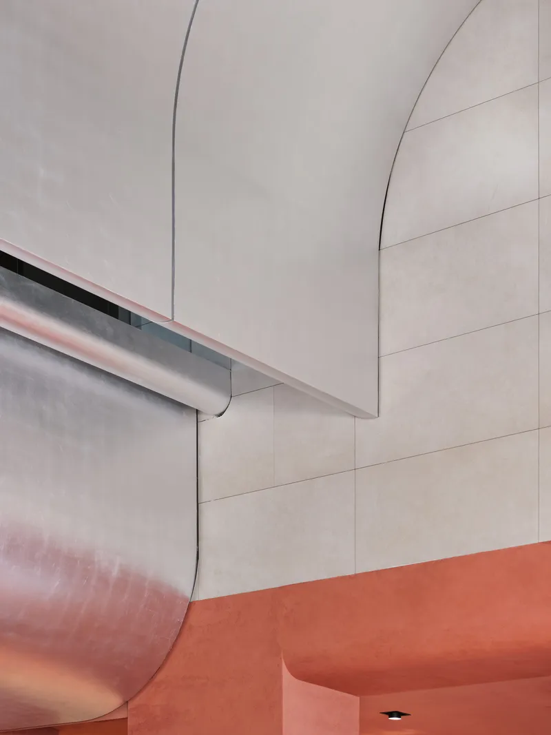 Detail of curved plaster wall forms with recessed lighting meeting an orange resin floor