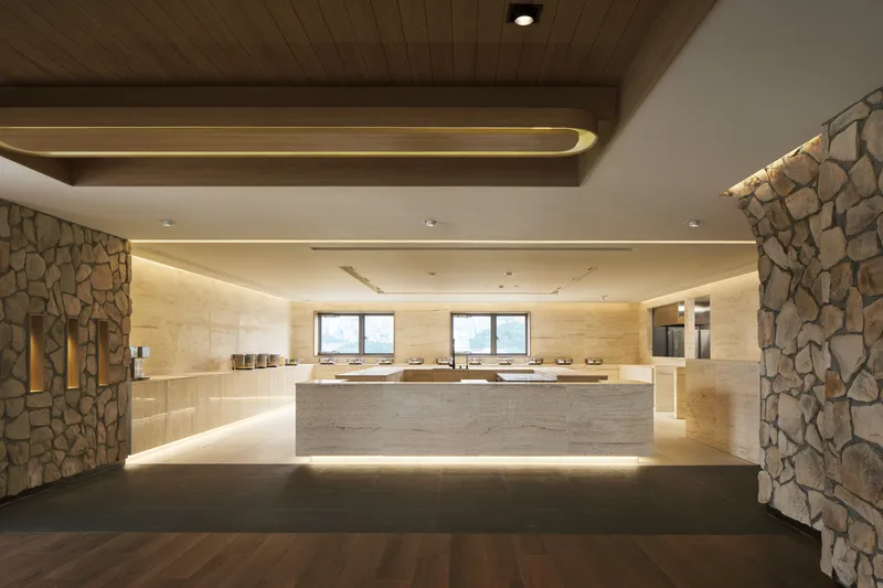 Reception hall with fieldstone columns, timber ceiling beams, and a backlit travertine service counter