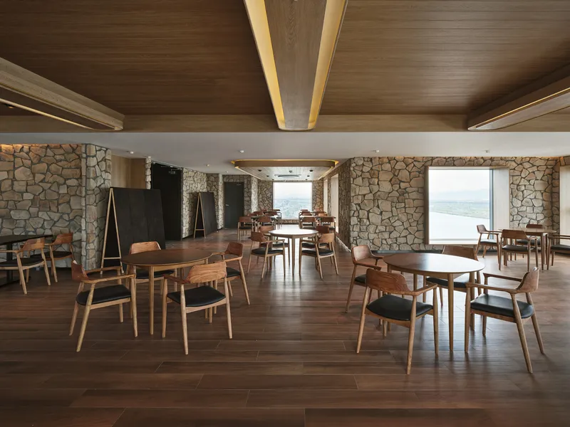 Dining room with fieldstone walls, timber ceiling beams, and oak furniture overlooking distant water views
