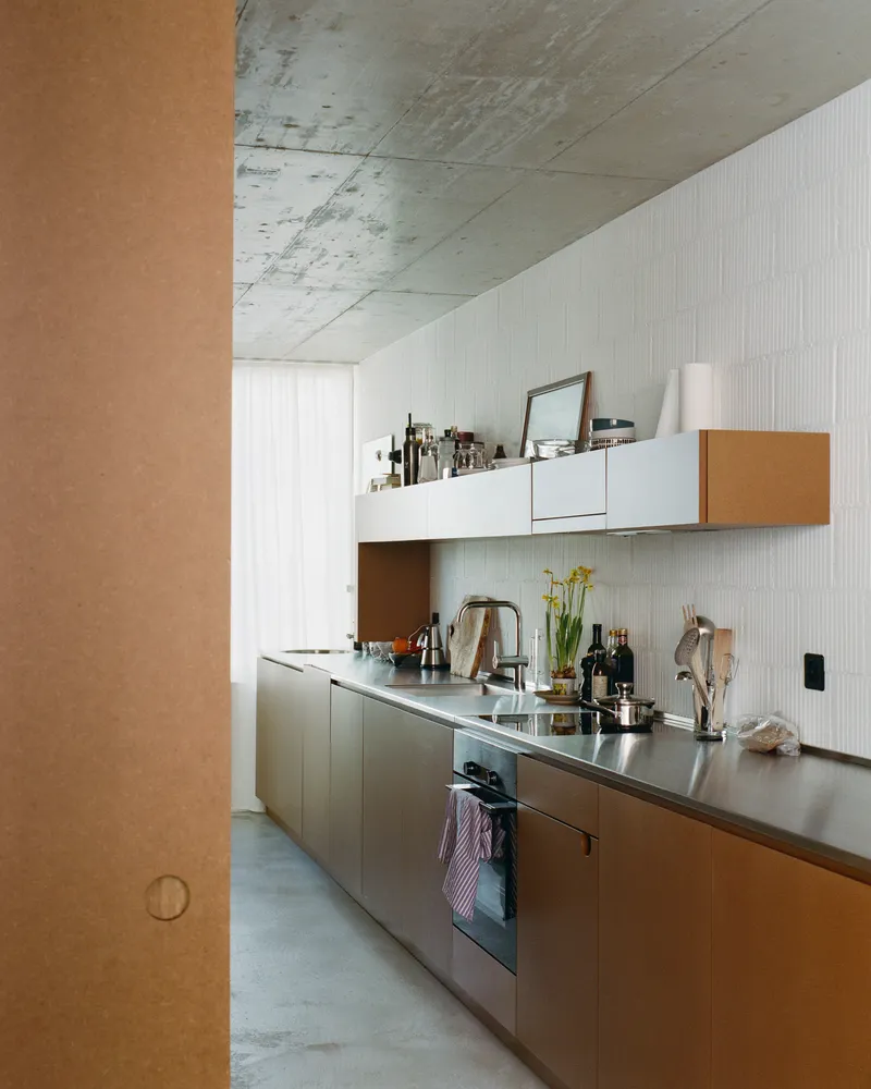 Galley kitchen with stainless steel countertops under an exposed concrete ceiling with daylight