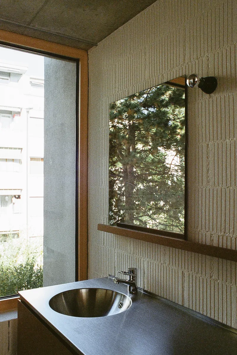 Bathroom vanity with circular steel sink below a window framing trees in afternoon light