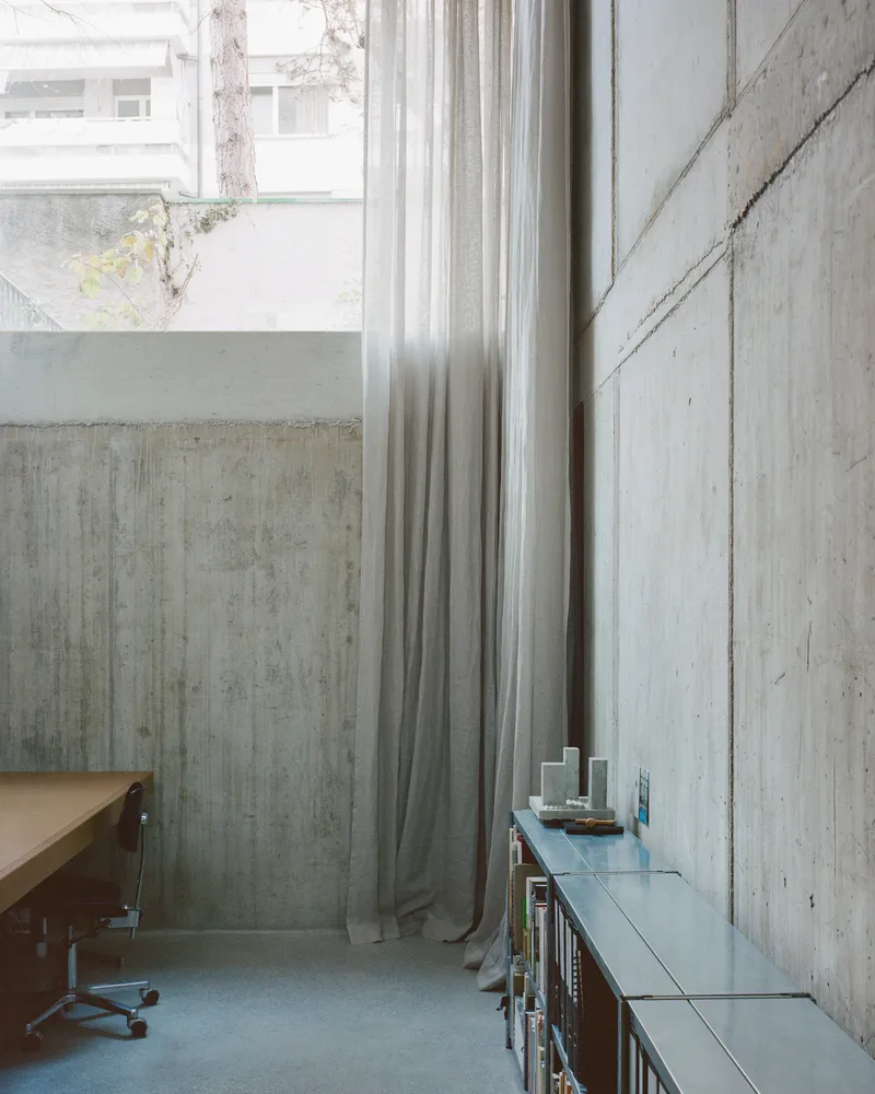 Concrete wall panels with floor-to-ceiling linen curtain beside a narrow office desk